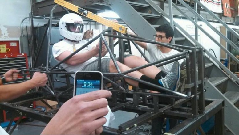 Driver seated in a Formula SAE cockpit prototype while the team evaluates the setup